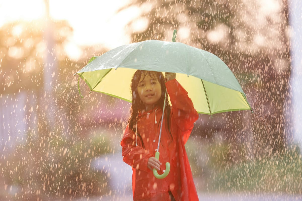 An asian girl in a red rain coat under a light green umbrella in the rain